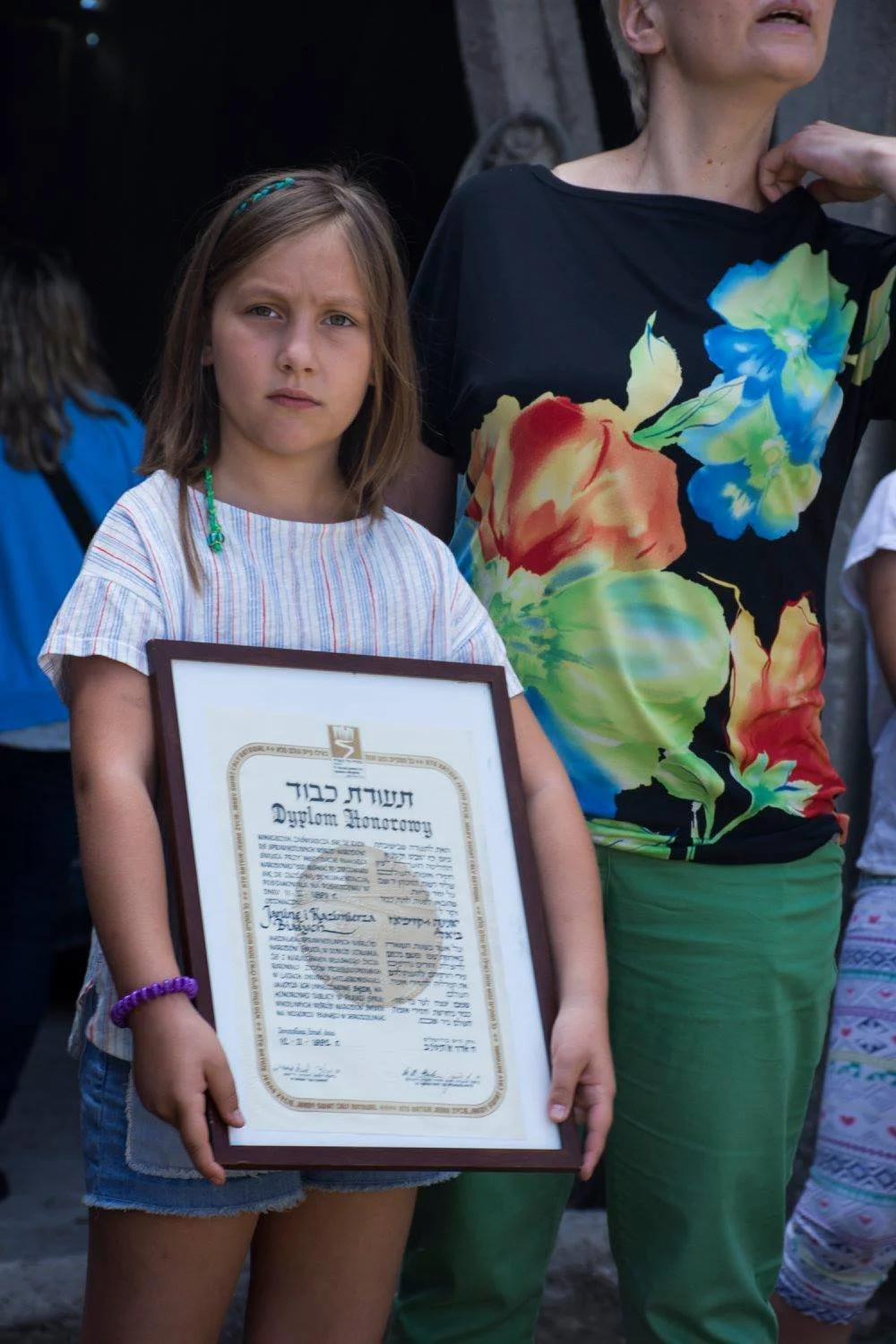 ילדה צעירה מחזיקה תעודת חסיד אומות העולם ממוסגרת בטקס משפחתי