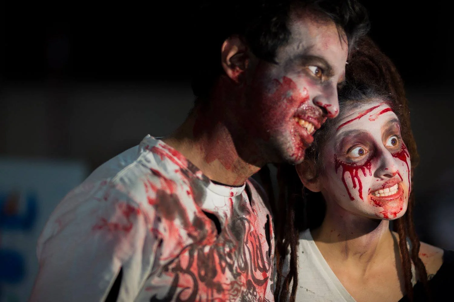 זוג מחופש לזומבים עם איפור מדמם מחייכים למצלמה עם פנים צבועות בלבן