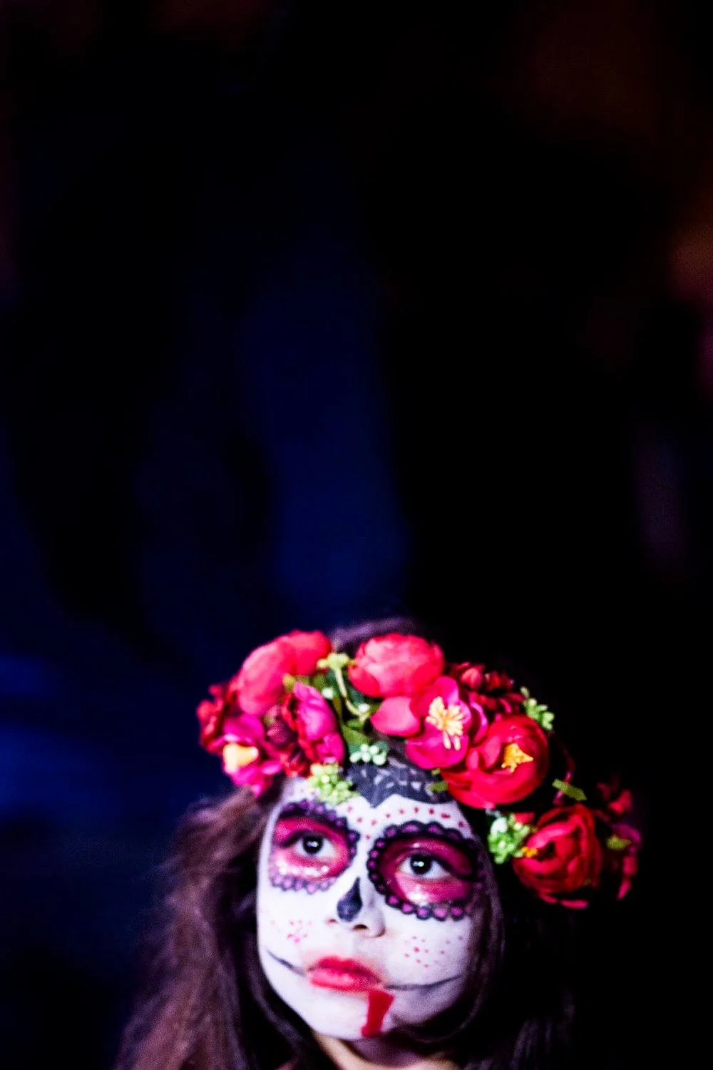 ילדה צעירה באיפור דייה דה לוס מורטוס עם כתר פרחים אדום בוהק