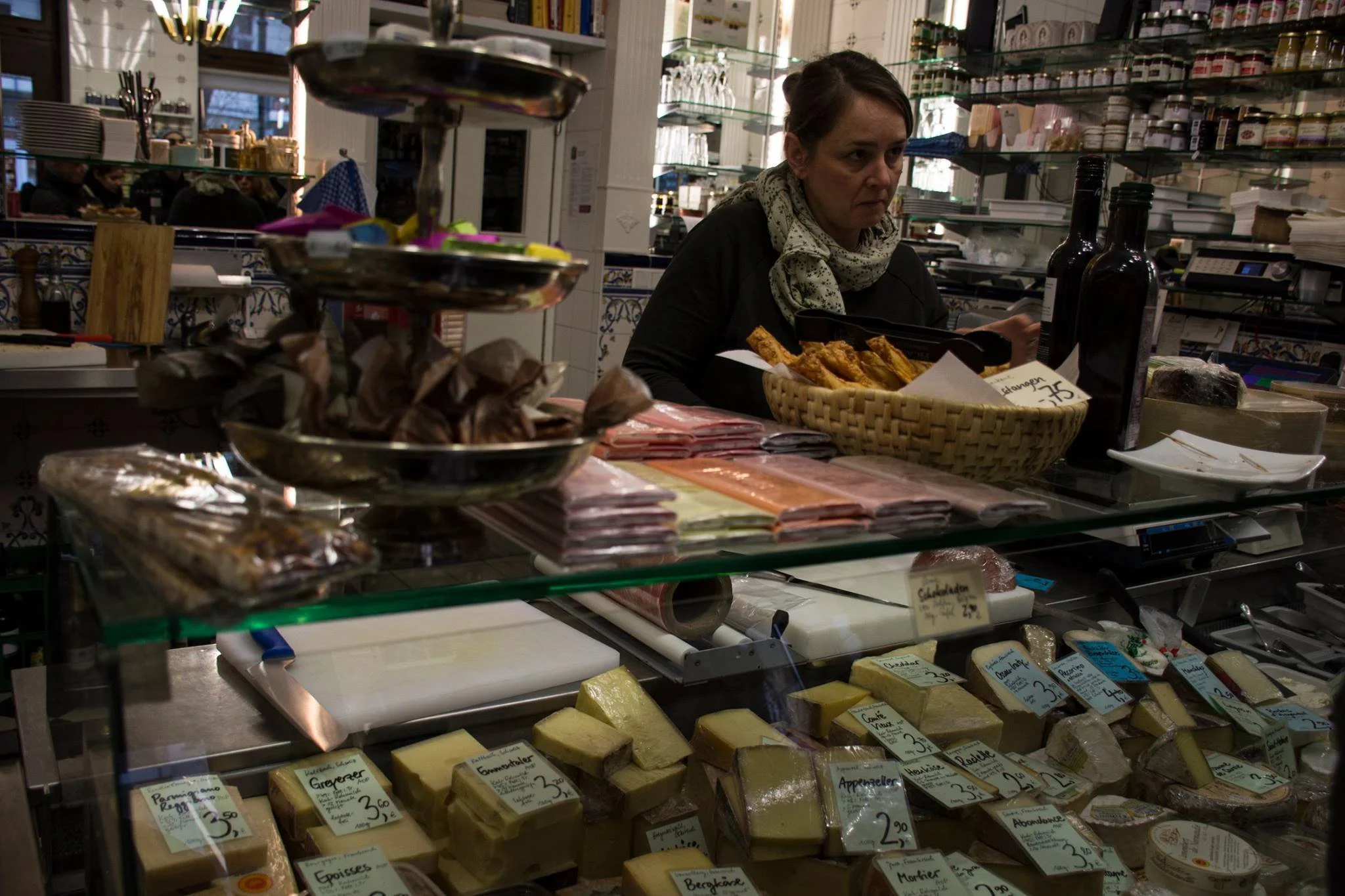 דלפק מעדנייה בשוק בברלין עם מוכר מאחורי ויטרינת זכוכית מלאה גבינות ונקניקים מיובשים