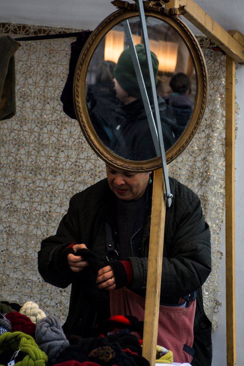 מוכר בשוק פשפשים משתקף במראה אובלית תוך כדי סידור בגדים בדוכן