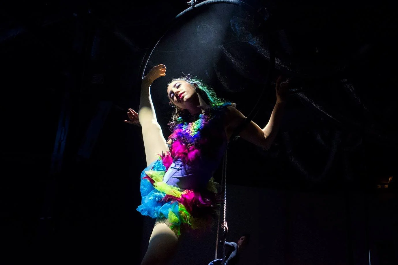 רקדנית אוויר בתלבושת נוצות צבעונית מצטלמת מתחת לזרקור על חבל