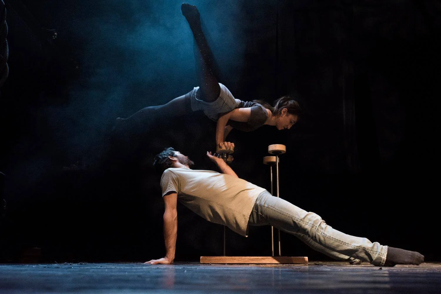 אקרובט זוגות מאזֵן על קנים בזמן שהפליירית קשתה מעליו באור במה מעושן