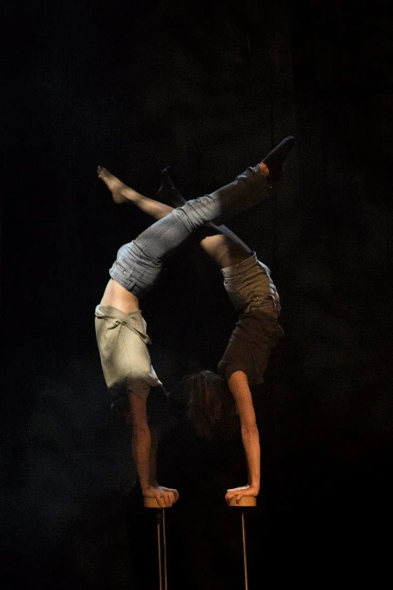 שני אקרובטים בעמידות ידיים מראה על קנים נפרדים, כפות הרגליים נפגשות מעל