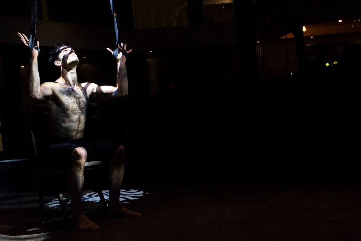 מבצע גברי מואר בזרקור, יושב עם ידיים מורמות וראש מוטה לאחור