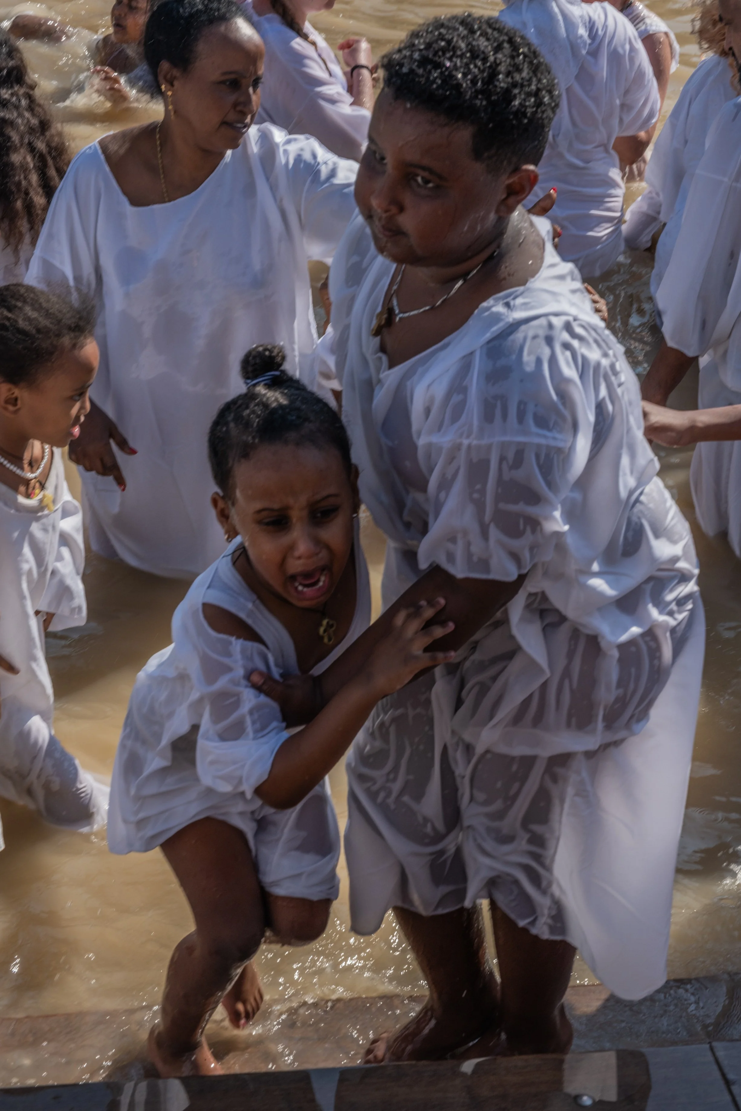 ילדה נצמדת לנער בלבן על שפת המים, צפיפות וטבילה ברקע