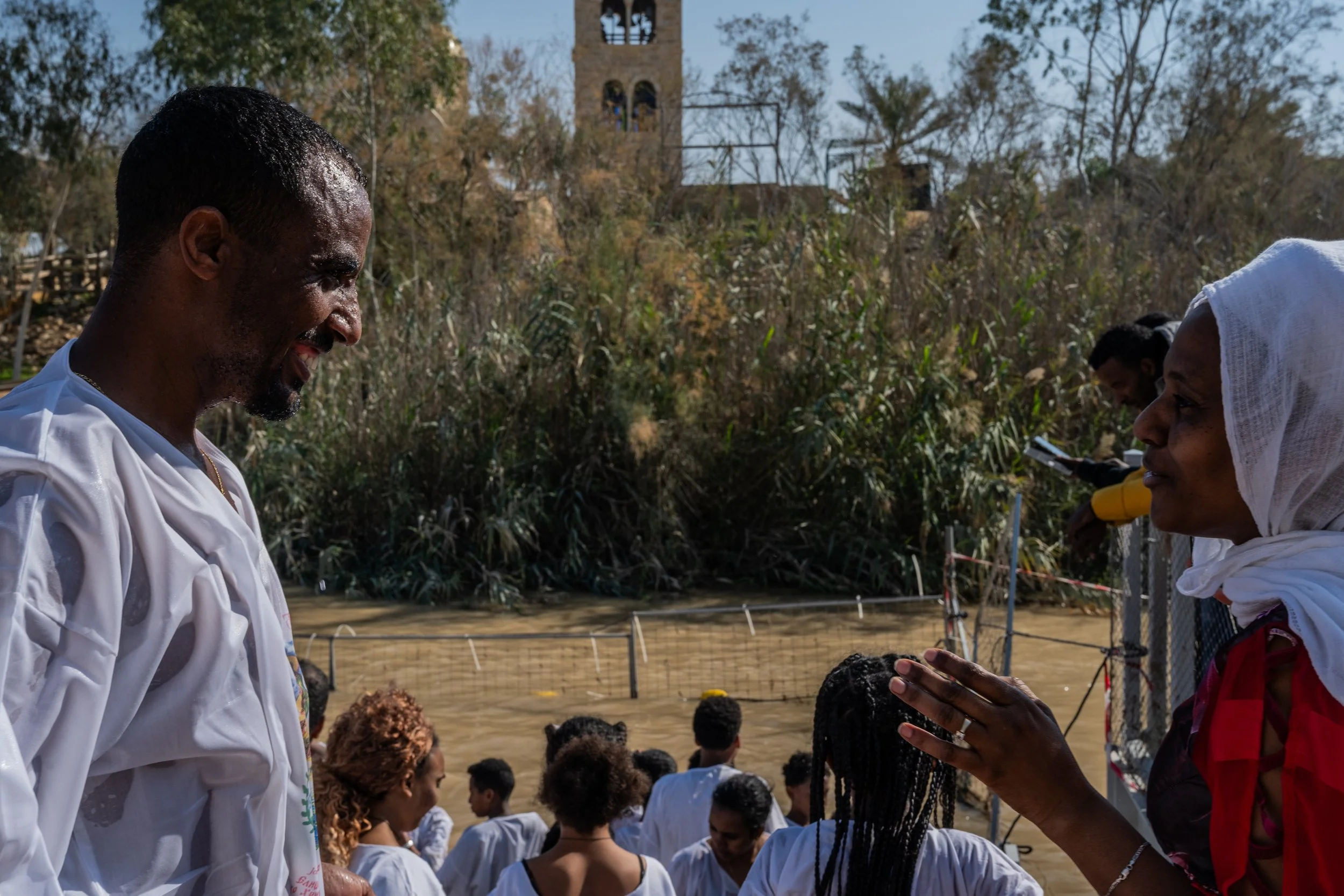 גבר בלבן פונה לאישה במטפחת אדומה, שיחה קצרה בתוך ההמון ליד הנהר