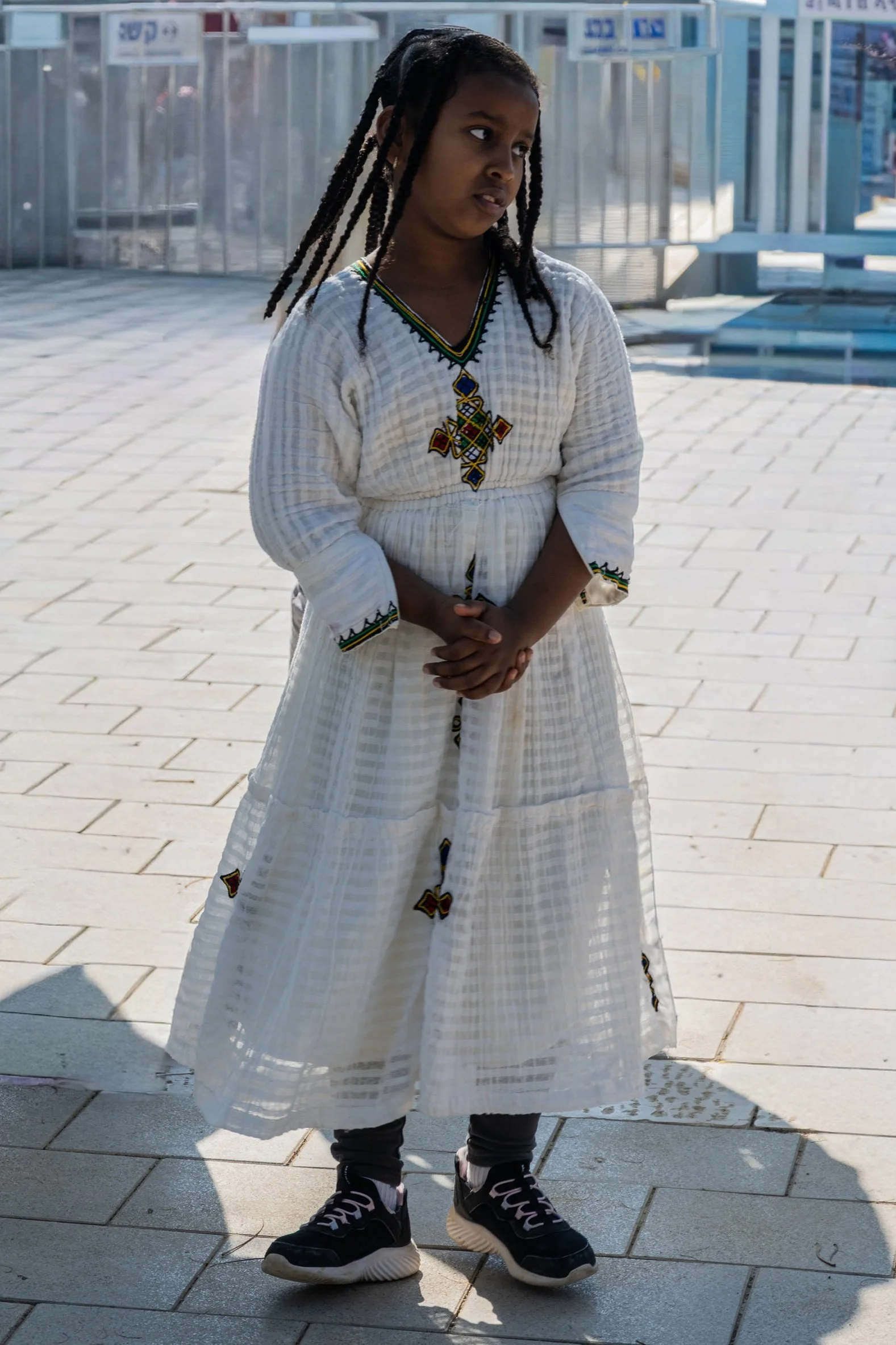 Girl in a white dress standing alone on the plaza at Qasr al-Yahud, wearing black sneakers