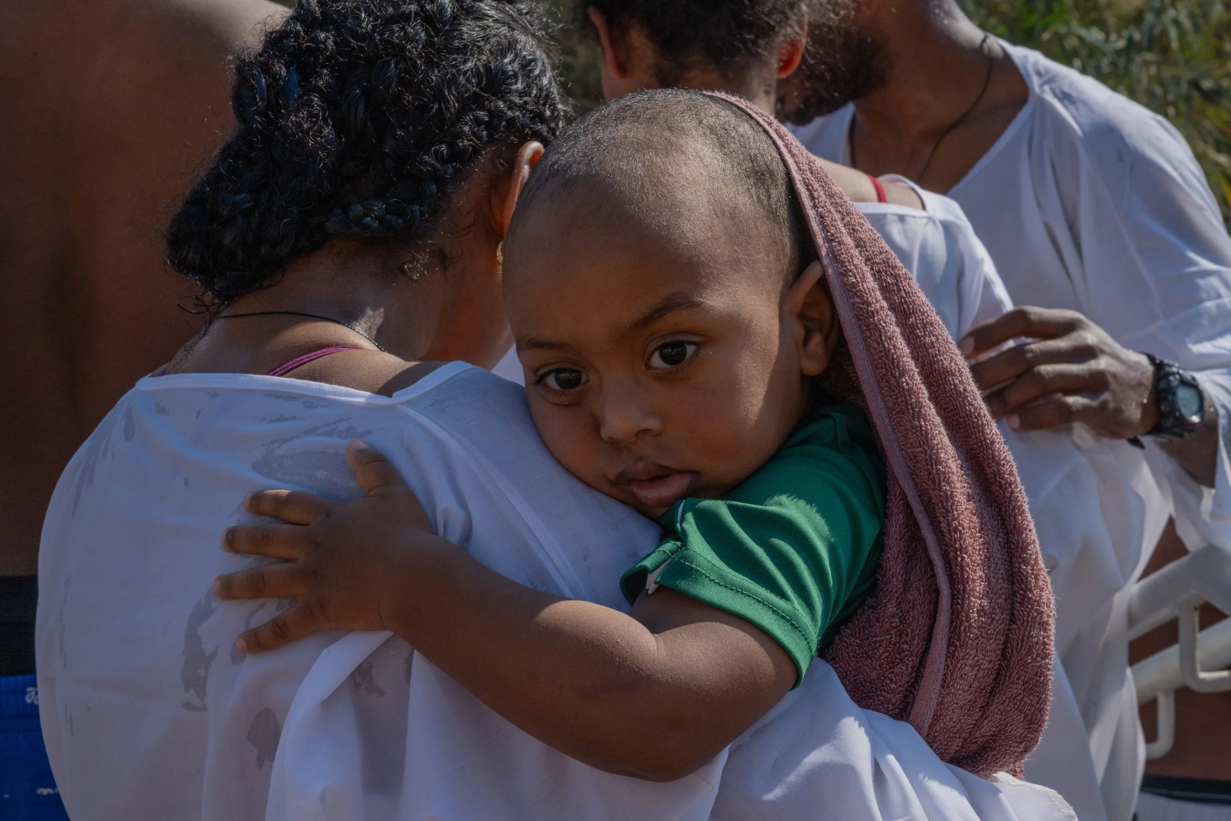 Child resting on an adult’s shoulder, looking toward the camera, a towel draped over their head