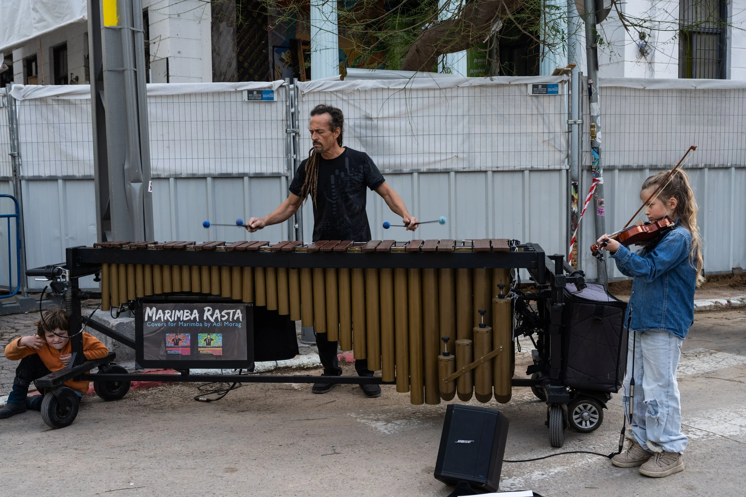 A young girl playing violin beside a street musician in the Carmel Market