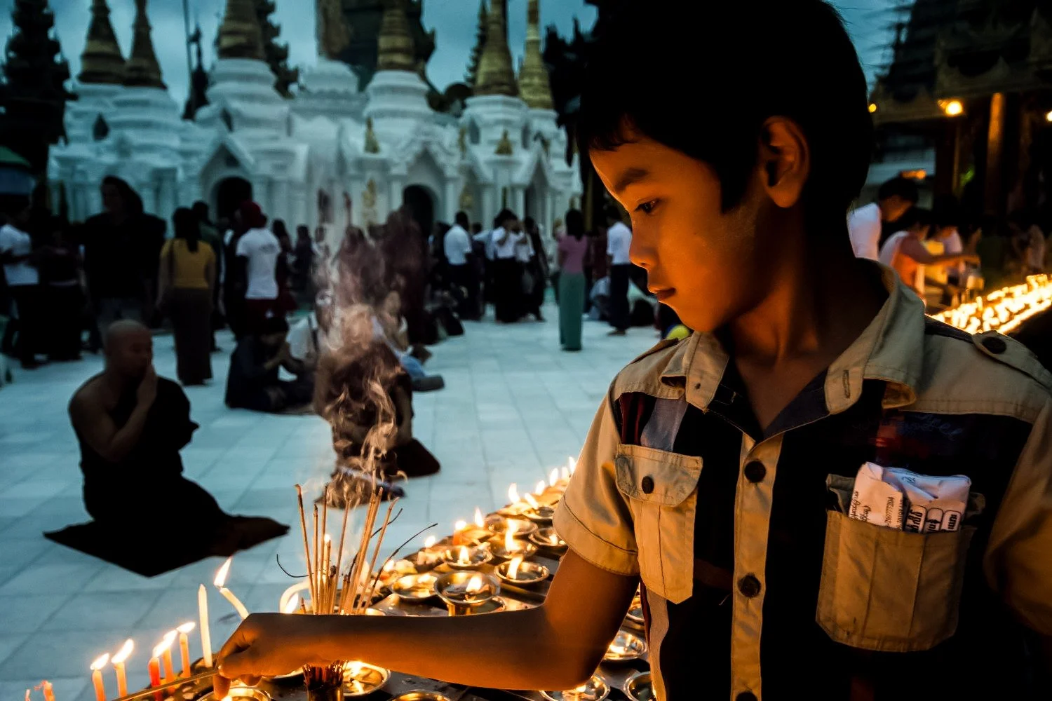 Boy lighting candles at a pagoda during the Thadingyut Festival in Myanmar, his face illuminated by warm candlelight