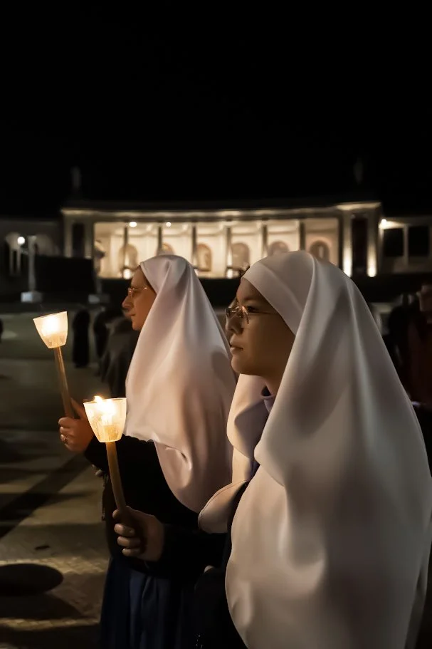 Two women in white veils holding lit candles during the candlelight procession in Fátima