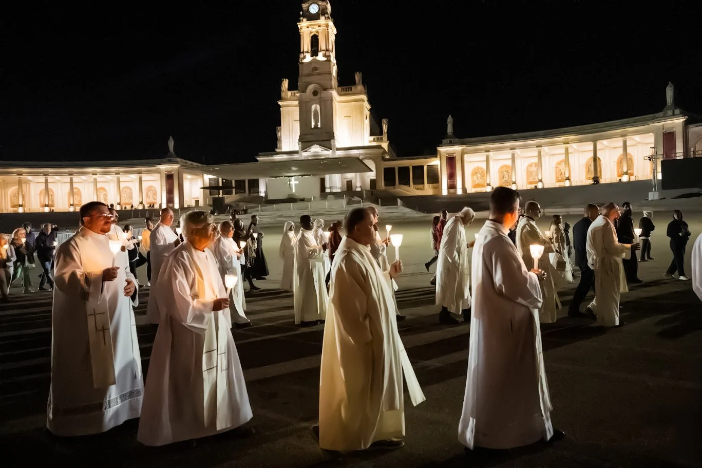 Clergy and pilgrims carrying candles across the sanctuary square at night in Fátima, Portugal