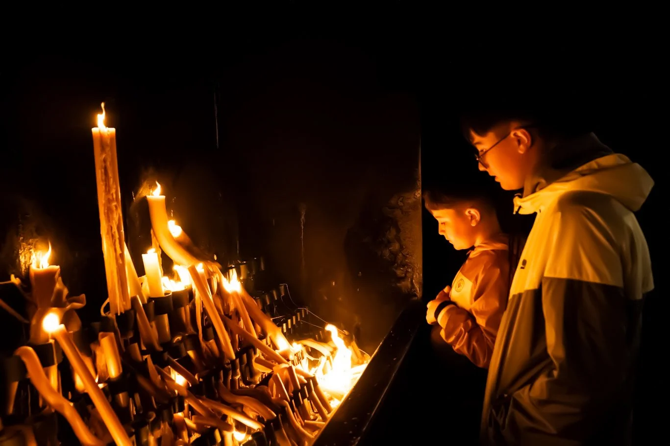 Children standing beside tall burning candles in a candle-offering space in Fátima