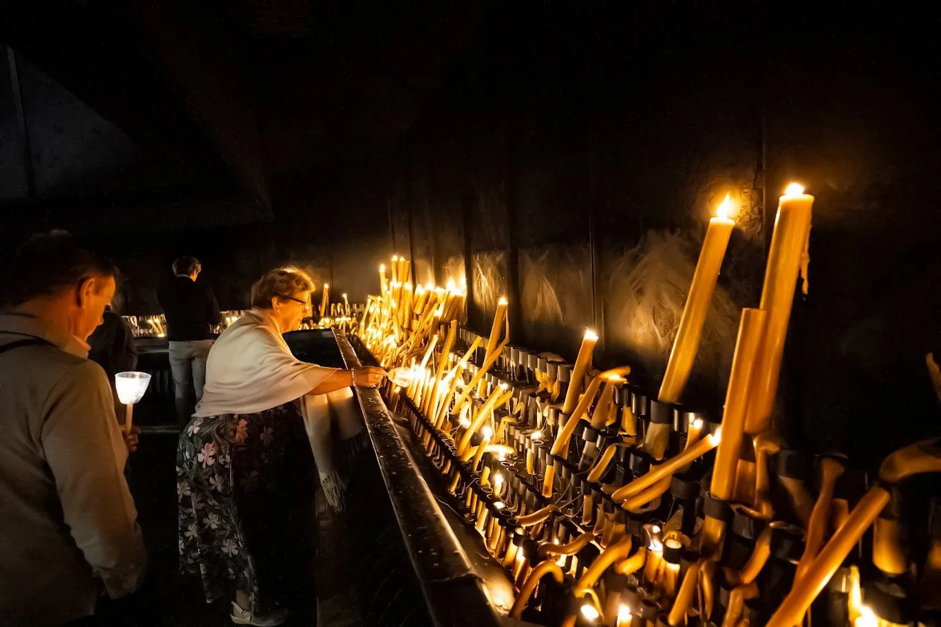 Visitors lighting tall candles in a large candle-offering area at the sanctuary in Fátima