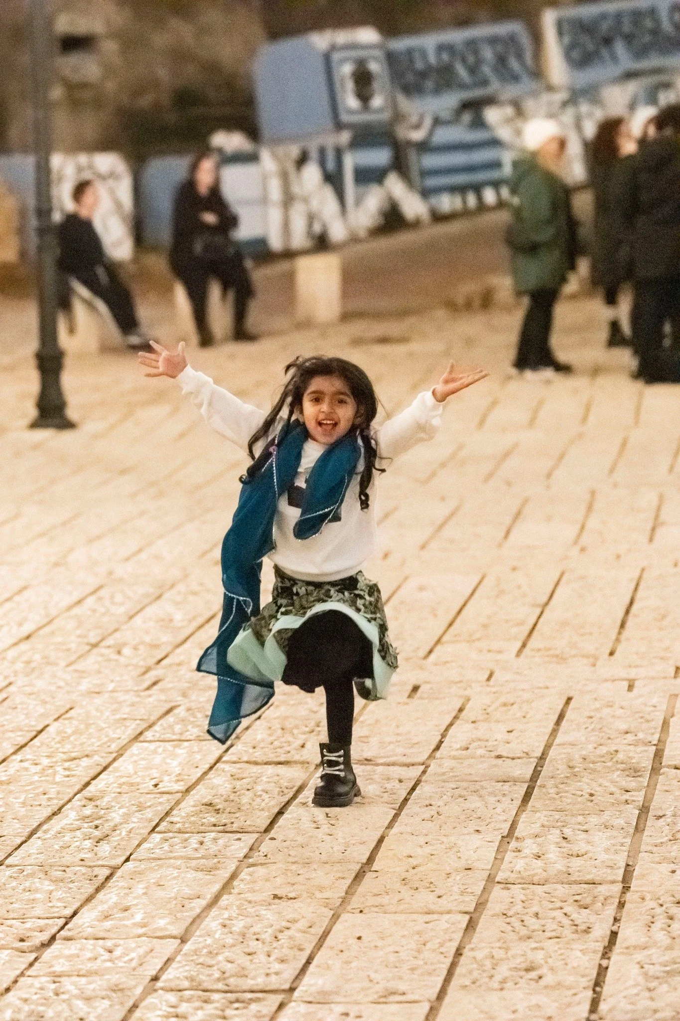 Child running joyfully across a stone plaza in Jaffa during Christmas festivities at night