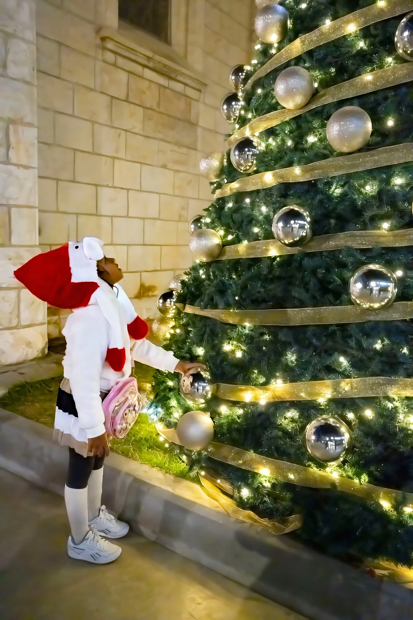 Young girl in a Santa hat standing beside a large decorated Christmas tree in Jaffa