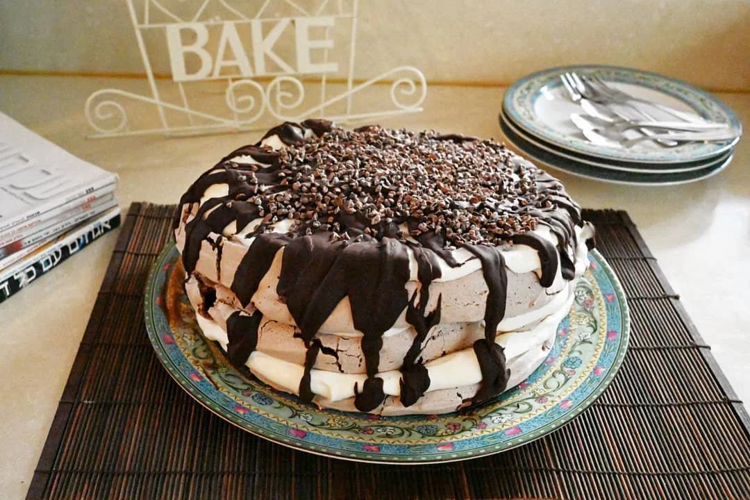עוגת מרנג גבוהה ברוטב שוקולד על צלחת וינטג' אהובה, מוכנה לאורחים ולקפה של שעות מאוחרות