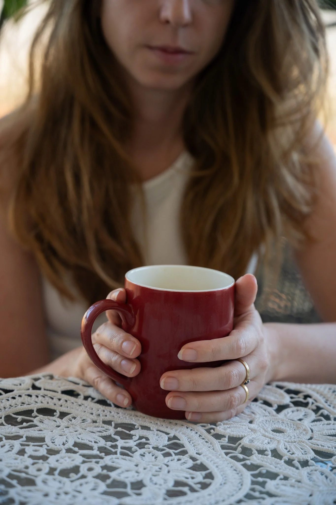 אישה מחזיקה ספל אדום מעל שולחן בעל דוגמת תחרה
