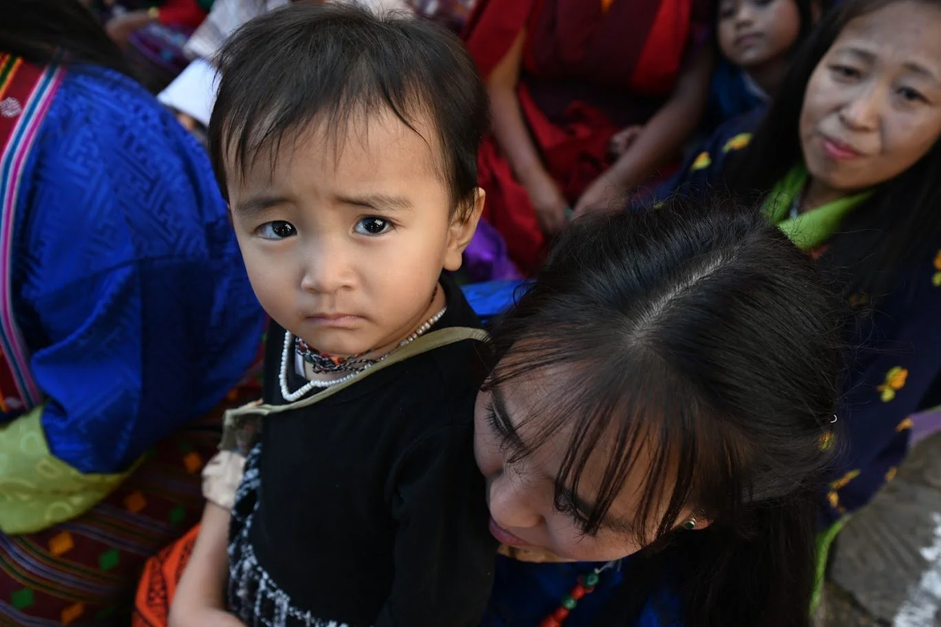 ילד קטן מביט למצלמה מעל כתפה של אישה בתוך המולת רחוב צפופה – בהוטן