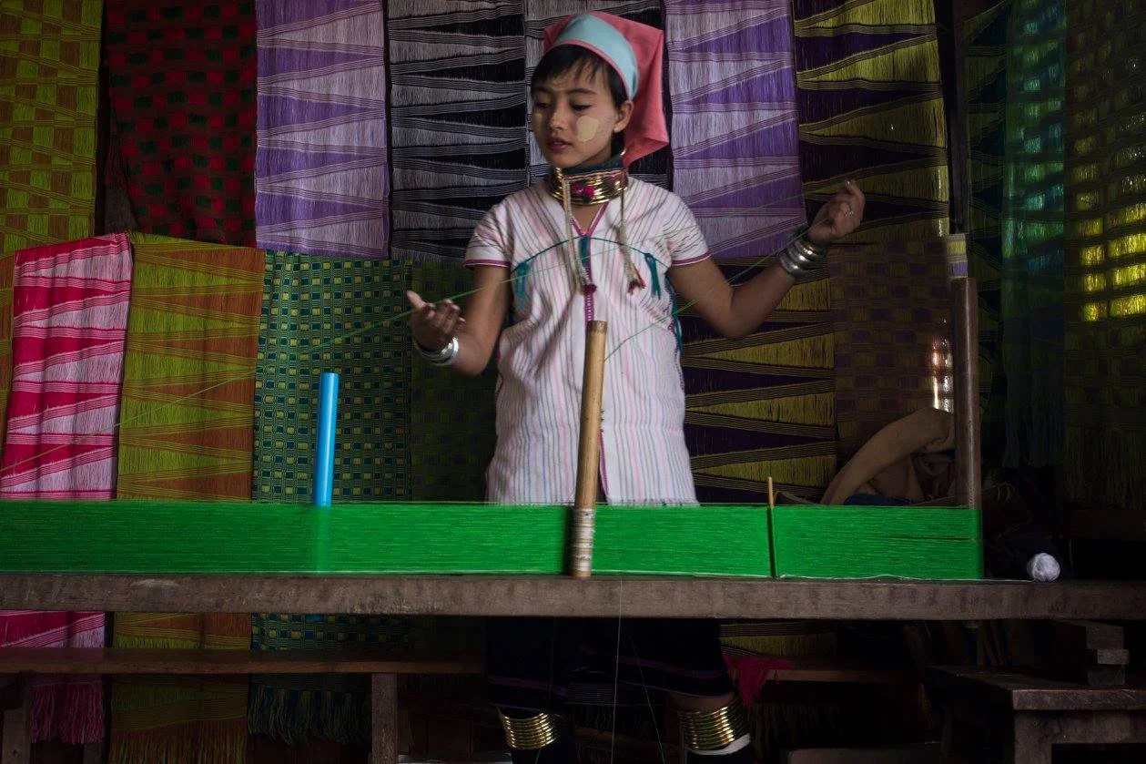 ילדה עומדת על במה קטנה בין בדים צבעוניים – אינלה, מיאנמר