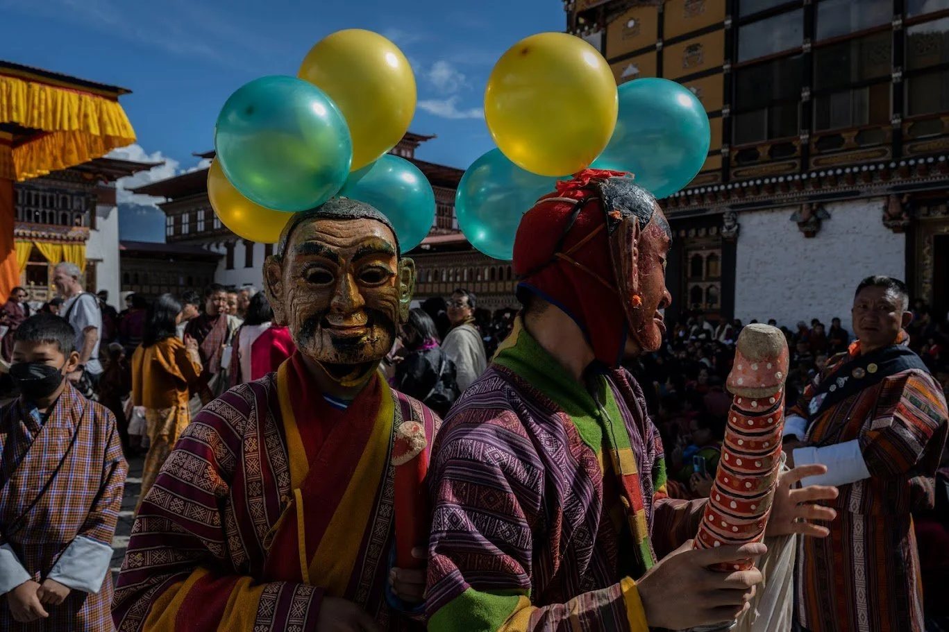 ליצני פסטיבל משתלבים בקהל עם בלונים ושובבות מקודשת, המסכות שלהם נושאות ברכות של צחוק ומזל – טימפו, בהוטן