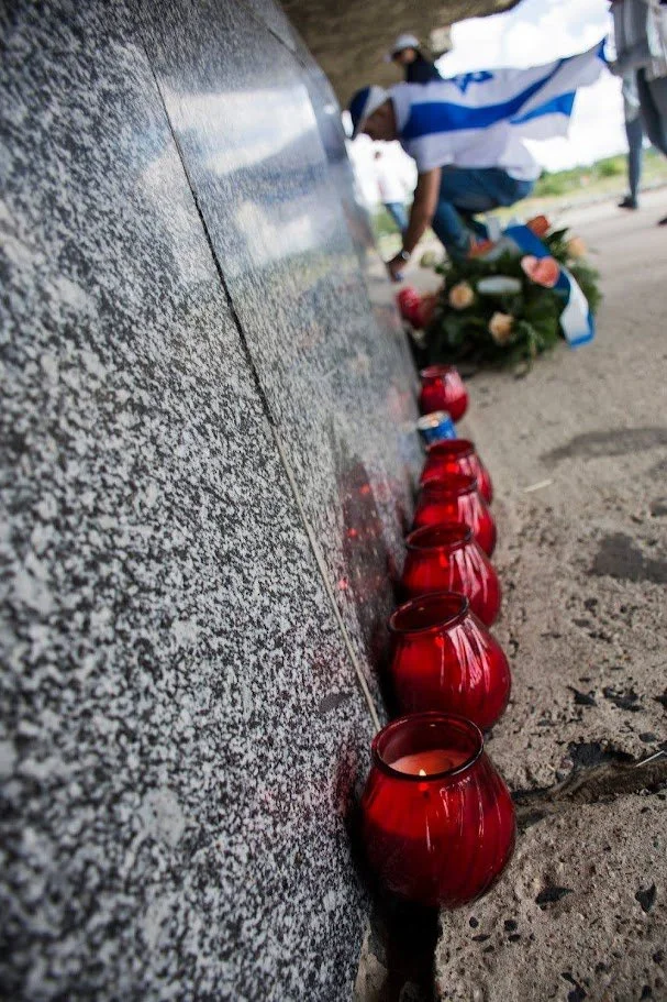 נרות זיכרון אדומים מסתדרים בשורה לאורך האבן, כשדגלים ופרחים מונחים בשקט של זיכרון – פולין