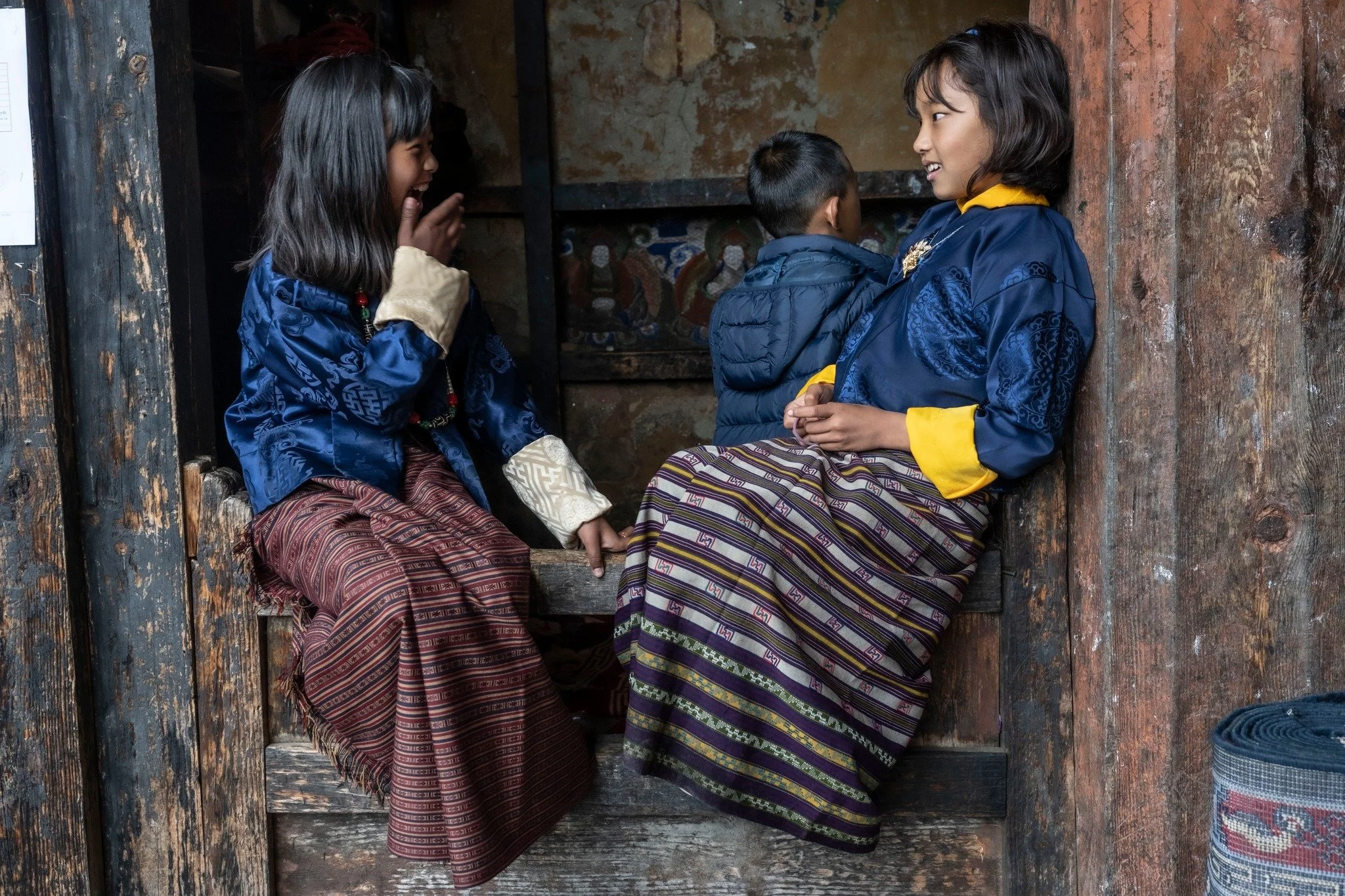 שתי ילדות בבגדים מסורתיים משוחחות בפתח בית בכפר – בהוטן