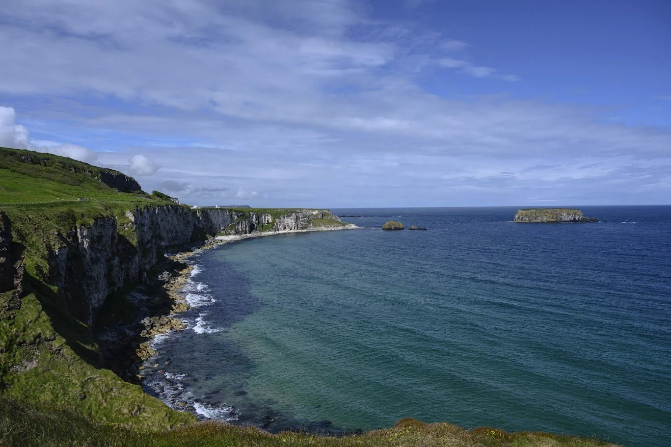 מפרץ טורקיז מוקף מצוקים ירוקים ושמיים כחולים זרועי עננים – צפון אירלנד