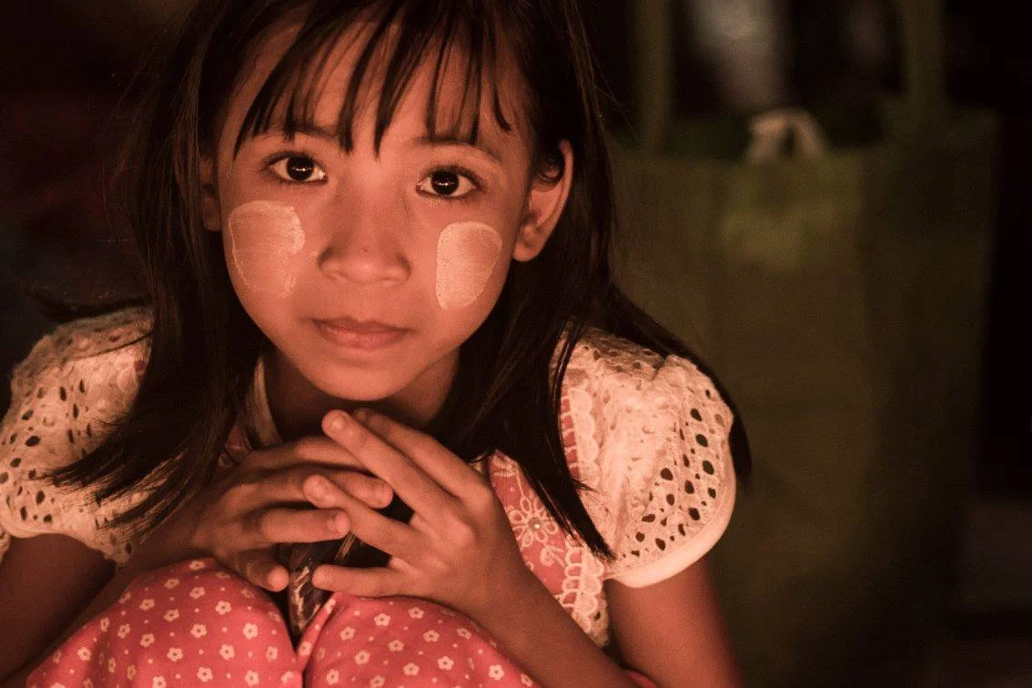 ילדה במבט תמים וחושש יושבת באור חם – מיאנמר