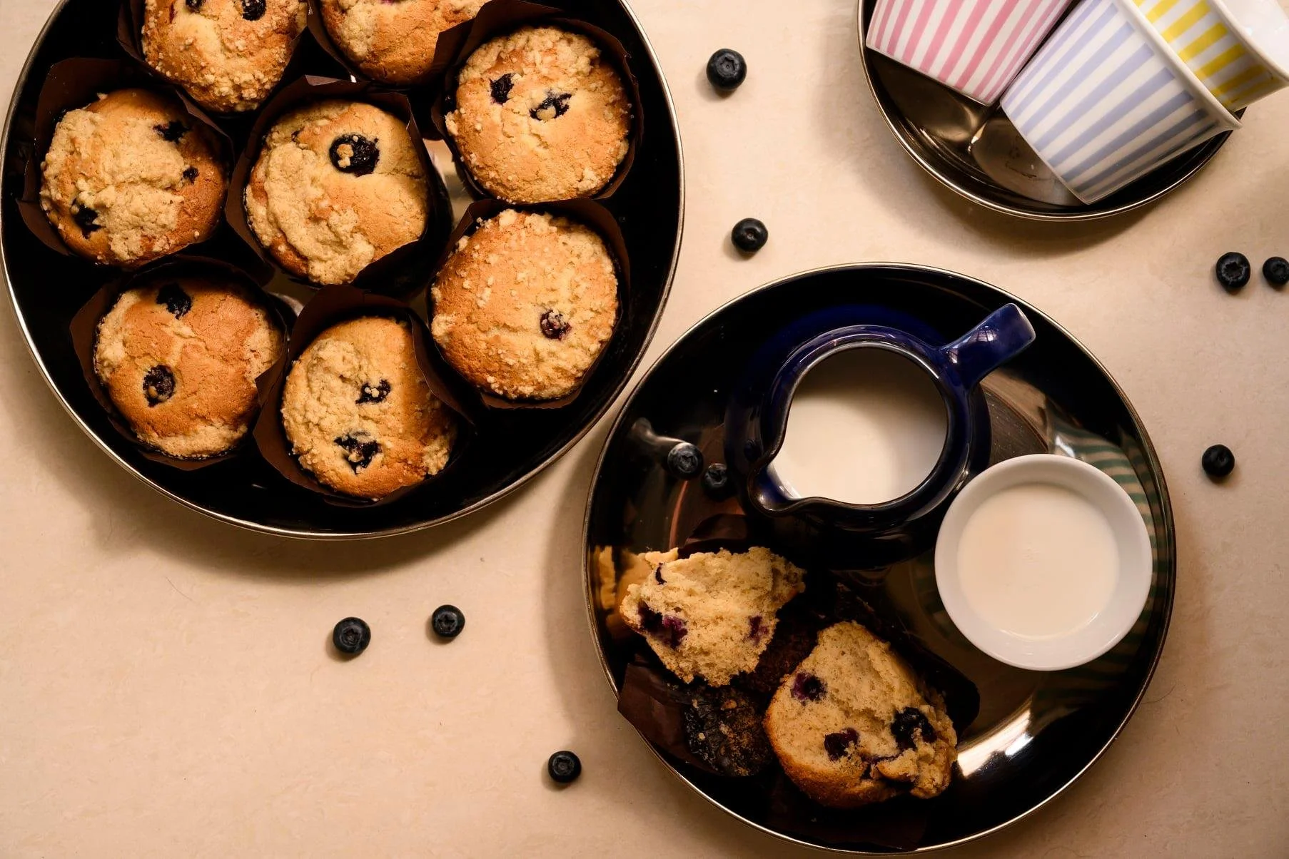 מאפינס אוכמניות שעדיין חמים, קנקן חלב, אוכמניות פזורות וכוסות פסים מסודרות בשורה בשביל החברים  שכבר בדרך