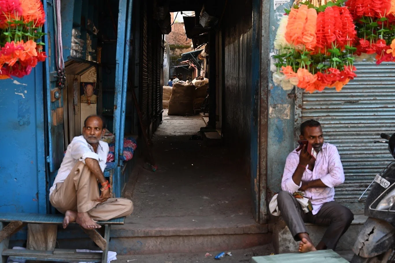גברים יושבים במעבר צר בין חנויות מקושטות בפנסים אדומים — דלהי, הודו