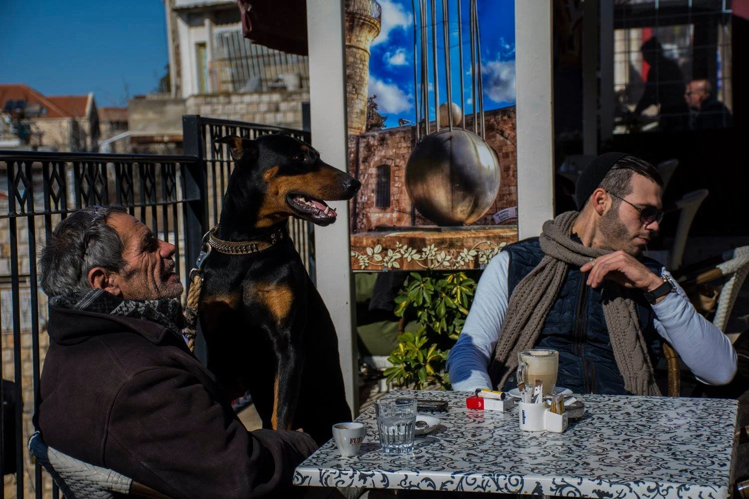 שני גברים וביניהם כלב שחור יושבים בבית קפה עירוני – נצרת, ישראל