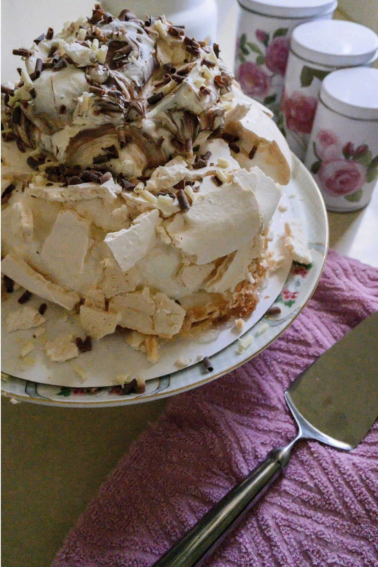 מרנג סדוק, סחרורי קצפת ותלתלי שוקולד נערמים לגובה לעוגת יום הולדת חגיגית ומעט מבולגנת