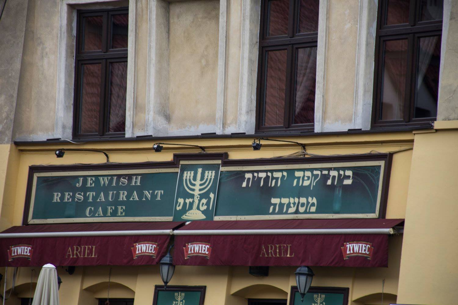 חזית "Jewish Restaurant Café" בקז׳ימיז׳ בקרקוב עם אותיות עבריות וסוככים אדומים