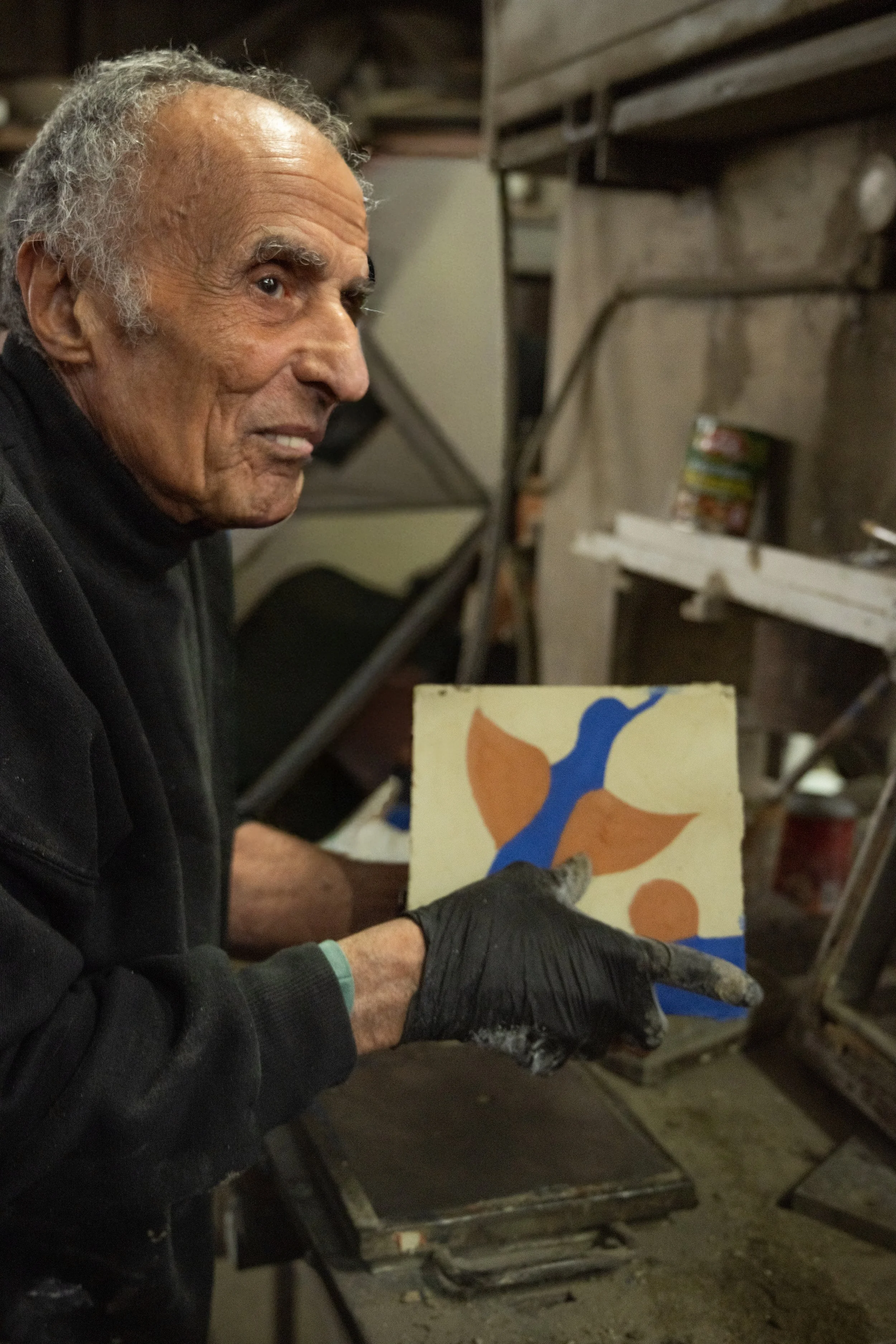 אבנר גלוסקא יוצר מרצפת מלט בעבודת יד, שופך שכבות חומר לתבנית על שולחן העבודה בסדנה.