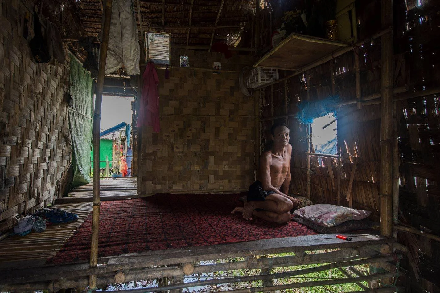 גבר יושב לבדו בתוך בית קש, אור אחר הצהריים נשפך פנימה – וייטנאם