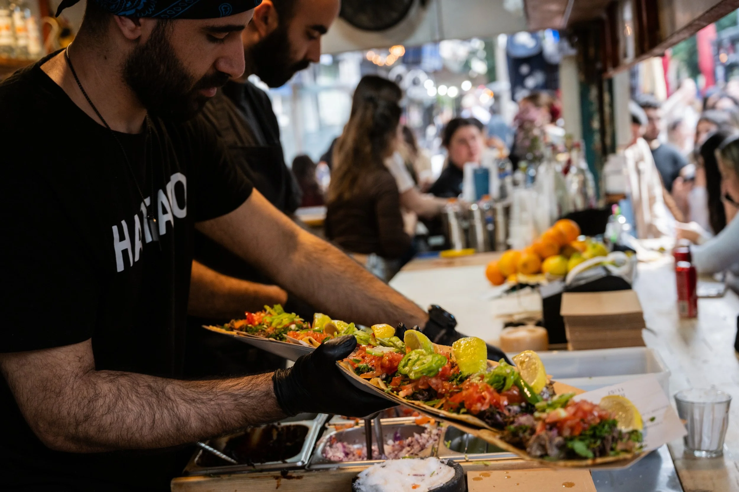 הכנת מנת טאקו ארוכה בדוכן אוכל בשוק הכרמל, ידיים עובדות מעל משטח עמוס מרכיבים
