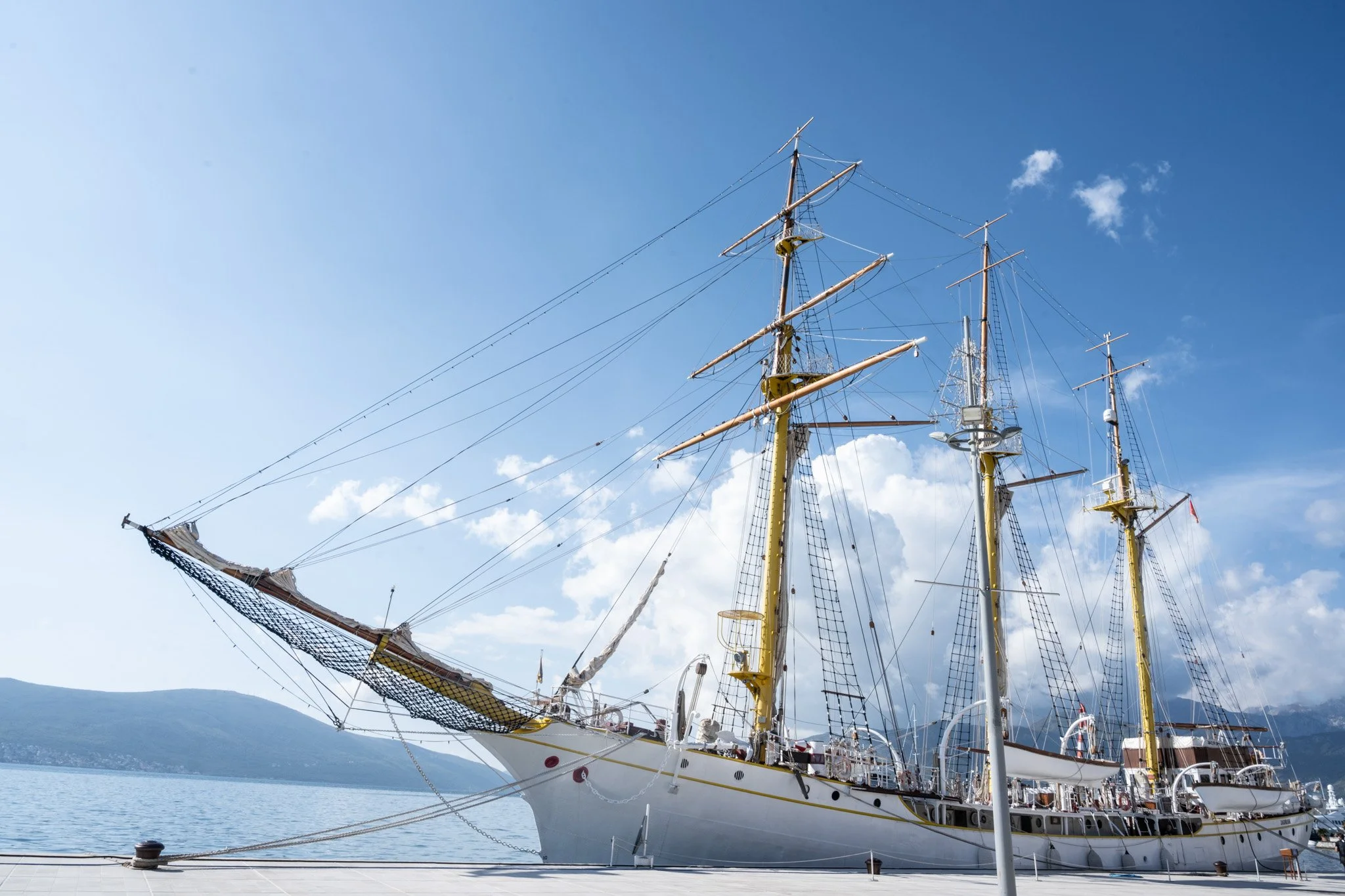 אוניית מפרש לבנה עם תורן גבוה עוגנת במים רגועים תחת שמיים בהירים – מונטנגרו