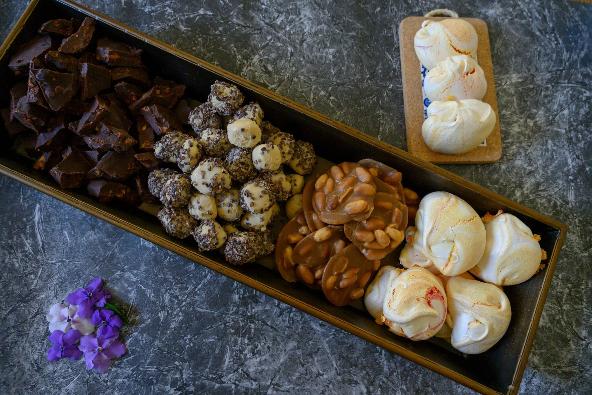 מגש ארוך של ממתקים ביתיים: שברי שוקולד, טראפלס שומשום, אשכולות קרמל ואגוזים ומקבץ מרנגים