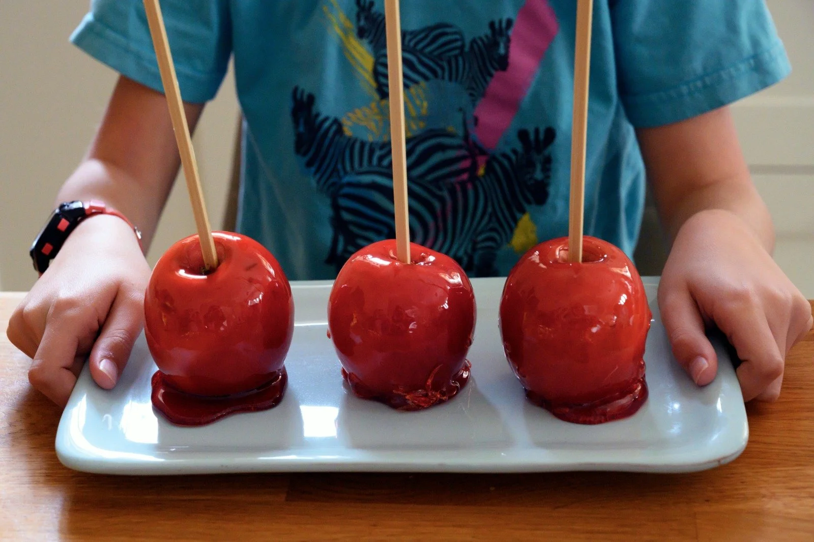 שלושה תפוחי סוכר מבריקים מוחזקים בזהירות בידיים קטנות – פינוק יריד תוצרת בית