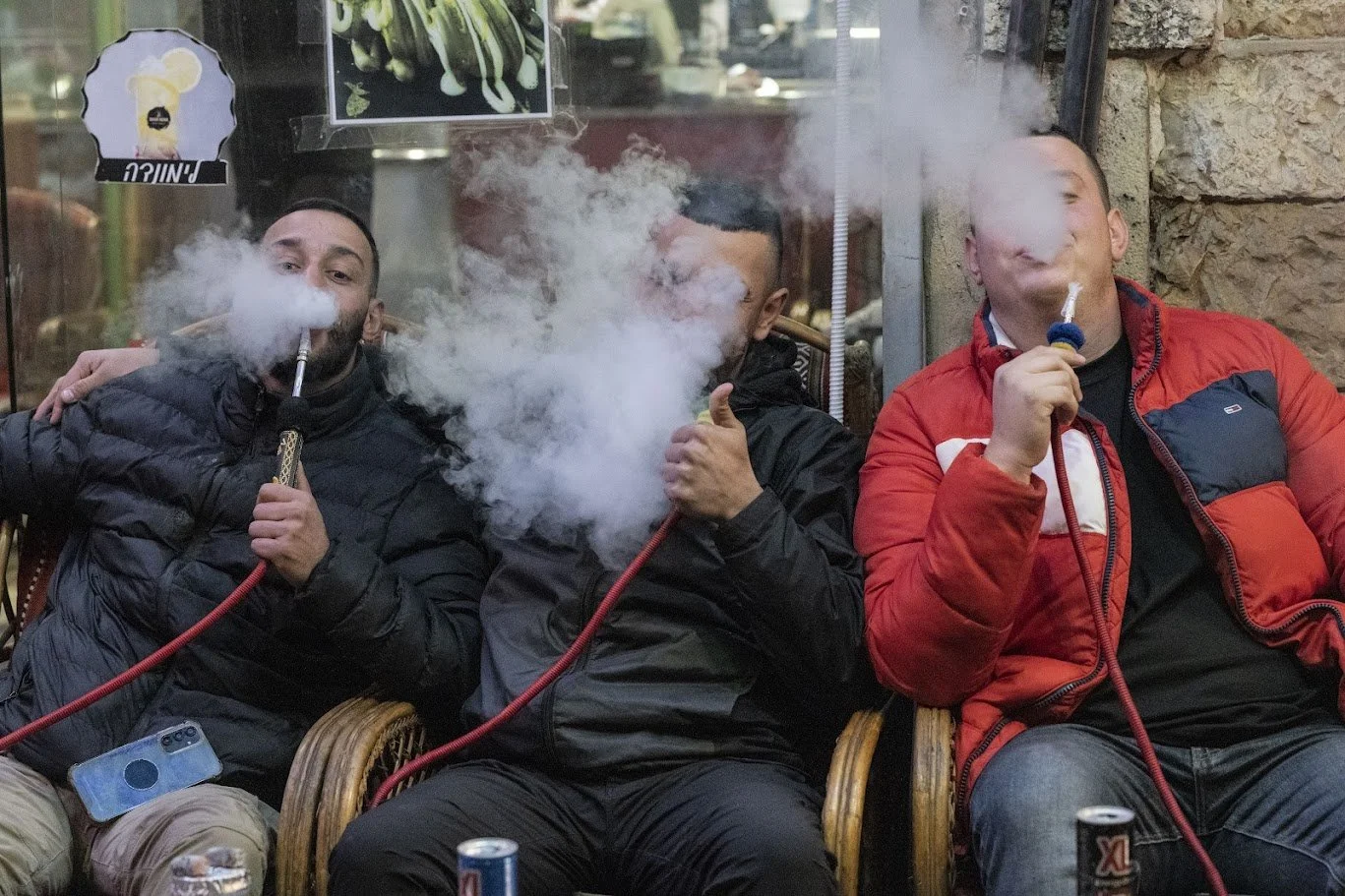 שלושה גברים יושבים בבר נרגילות, ענני עשן מסתלסלים סביבם ומטשטשים את פניהם – יפו, ישראל