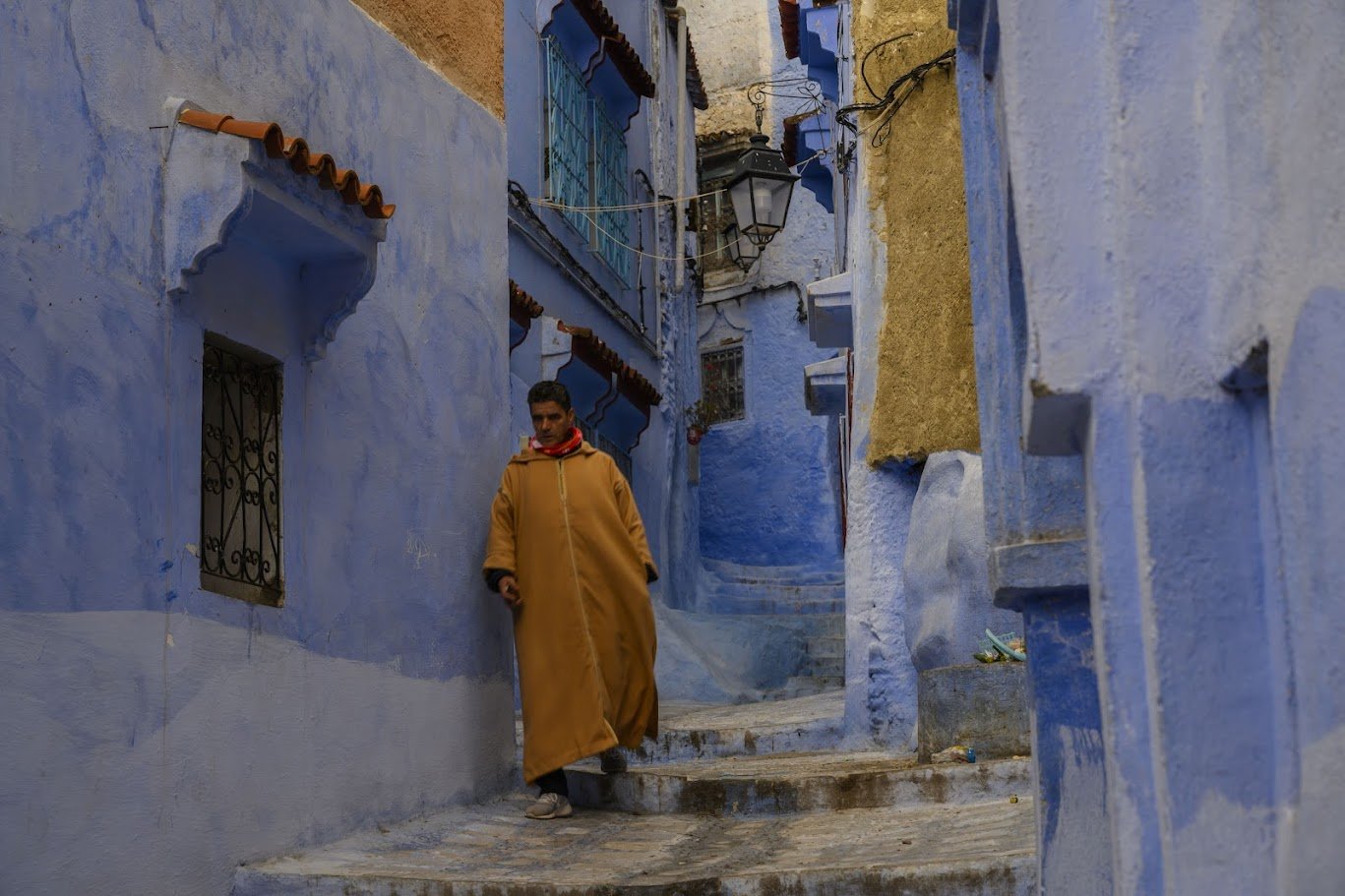 סמטה כחולה עם איש בגלימה צהובה יורד במדרגות — שפשואן, מרוקו
