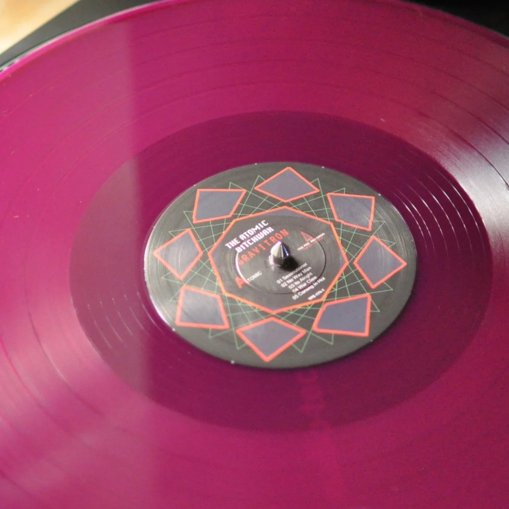 A purple vinyl record spinning on a turntable with a black label featuring red geometric patterns and text.