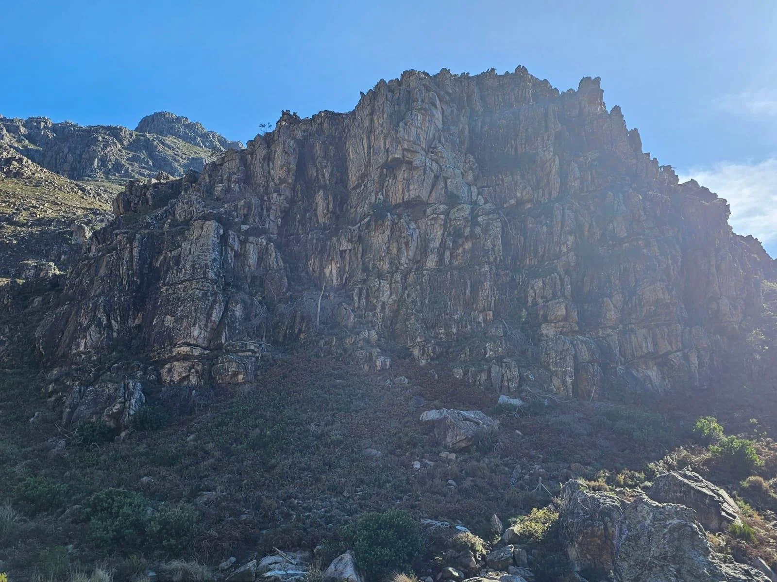 A rocky mountain with steep cliffs and sparse vegetation under a clear blue sky.