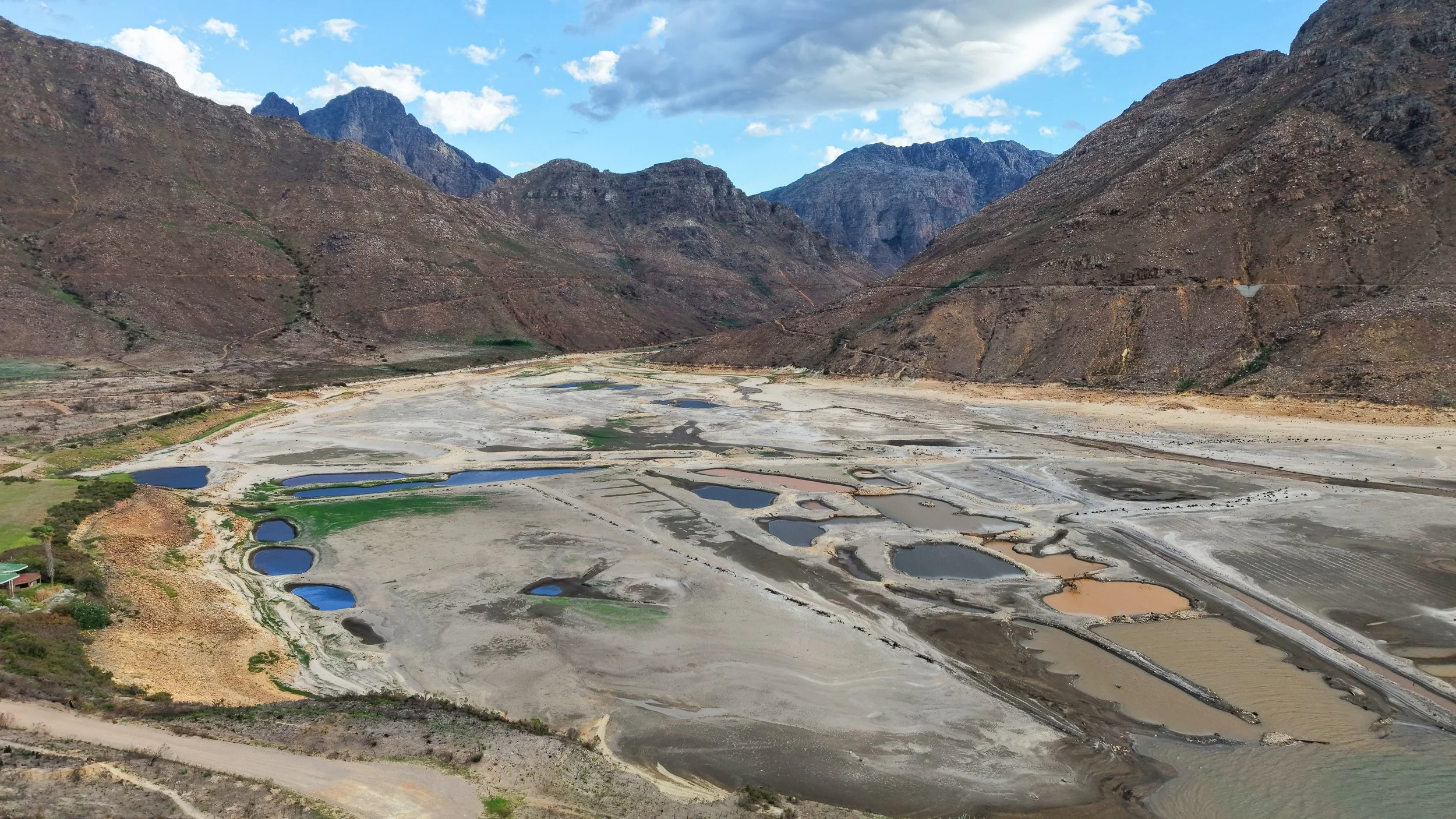 Barren landscape in a valley with small lakes, surrounded by mountains and cloudy sky.