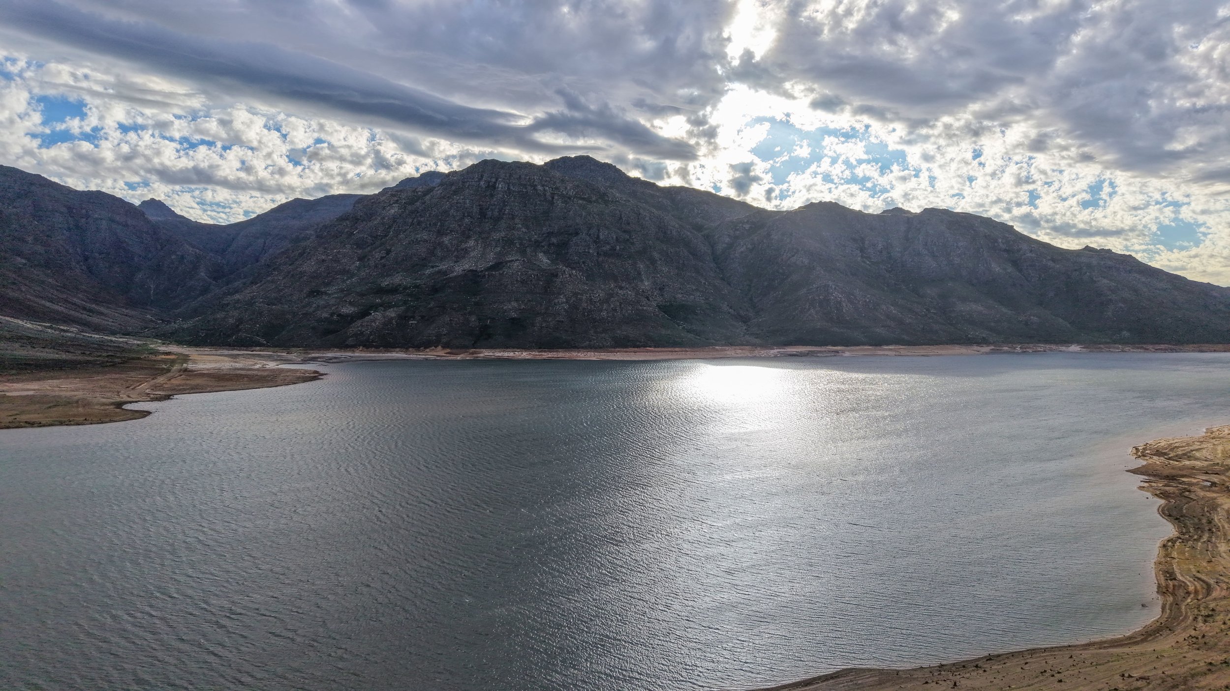 A large body of water with mountains in the background and a partly cloudy sky.