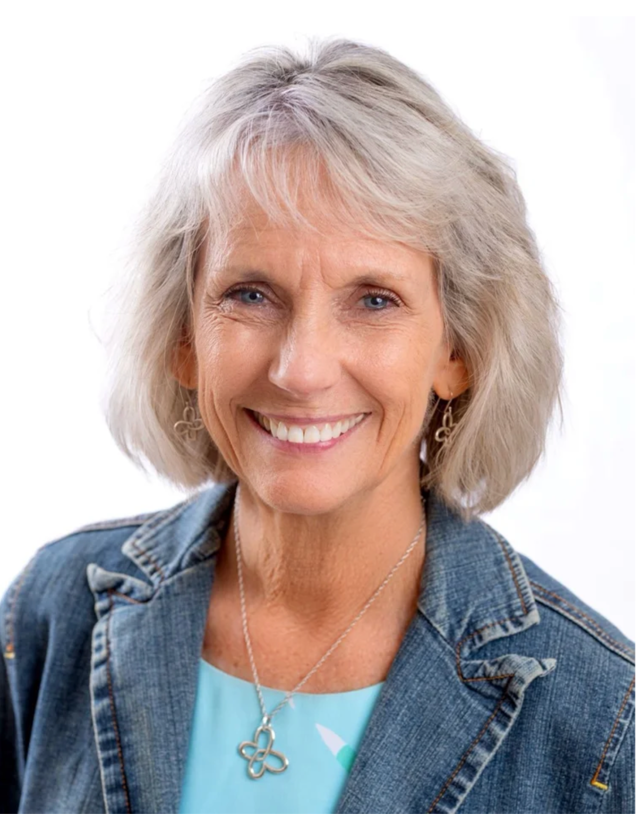 Woman with shoulder length white hair and a denim jacket smiling at the camera