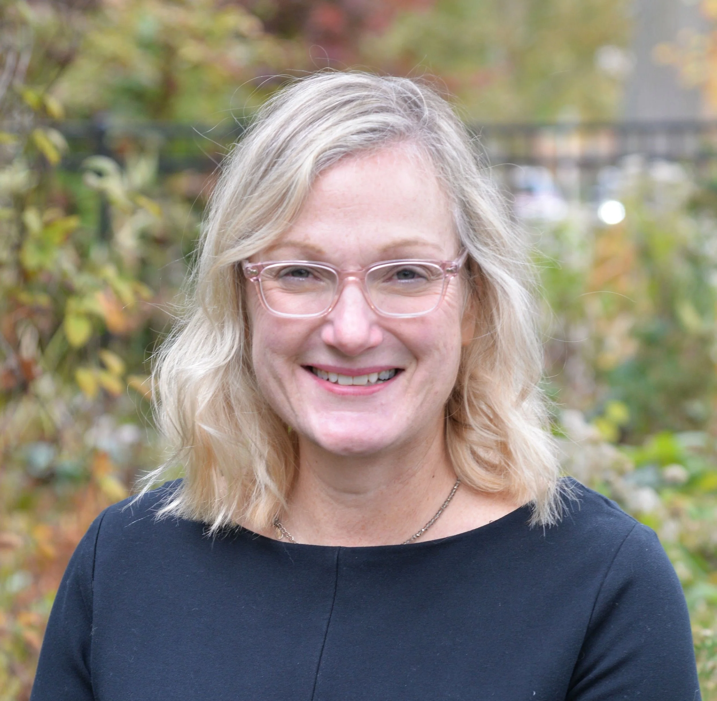 Woman with shoulder length blonde hair and a black shirt and glasses smiling at the camera