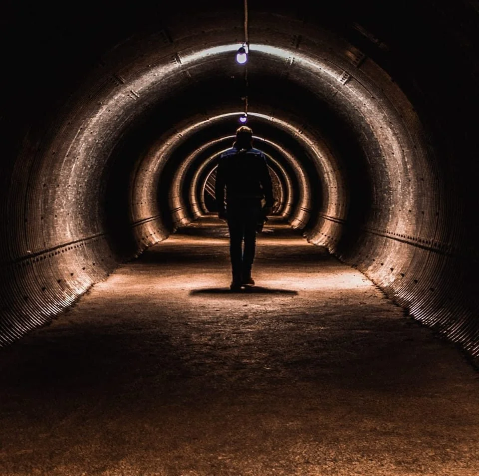 Une personne marche dans un tunnel métallique éclairé par des lampes suspendues au plafond.